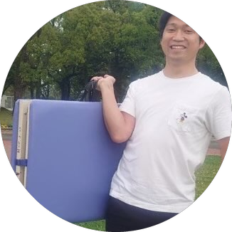 折りたたんだ施術ベッドを持って屋外に立つ院長